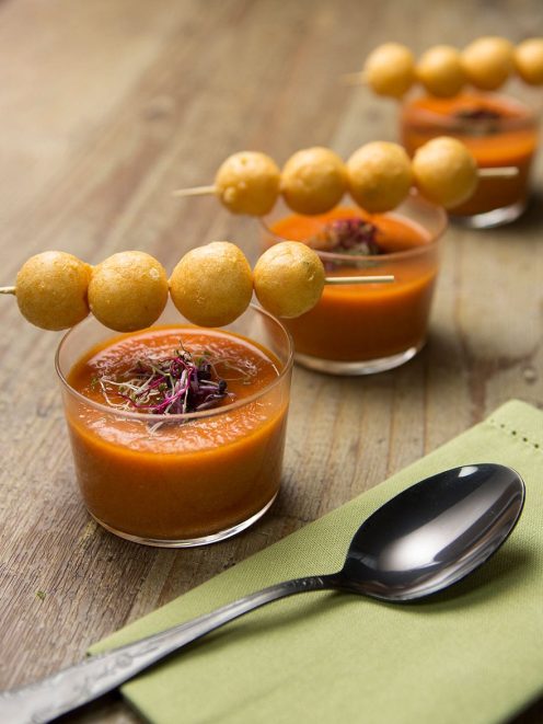 Meringhe salate con gazpacho servito in bicchiere, guarnito con microgreens e spiedino di palline dorate