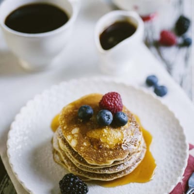 Pancakes senza glutine e latticini impilati con sciroppo dorato, mirtilli, lampone e mora