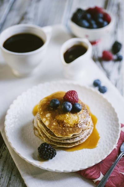 Pancakes senza glutine e latticini impilati con sciroppo dorato, mirtilli, lampone e mora