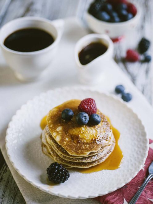 Pancakes senza glutine e latticini impilati con sciroppo dorato, mirtilli, lampone e mora