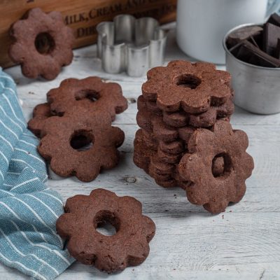Canestrelli al cioccolato a forma di fiore con foro centrale, impilati e sparsi sul piano