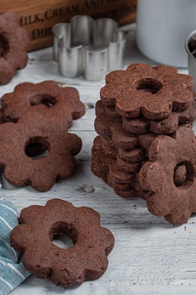 Canestrelli al cioccolato a forma di fiore con foro centrale, impilati e sparsi sul piano