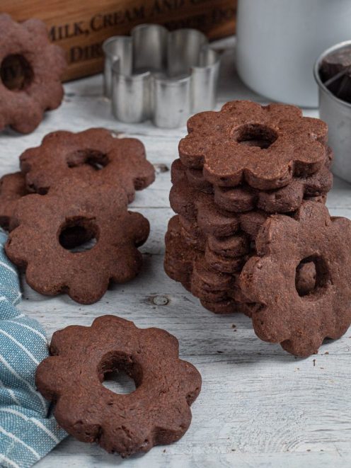 Canestrelli al cioccolato a forma di fiore con foro centrale, impilati e sparsi sul piano