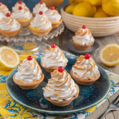 Frolle meringate al limone con ciuffi di meringa dorata e ribes rosso sopra crema al limone