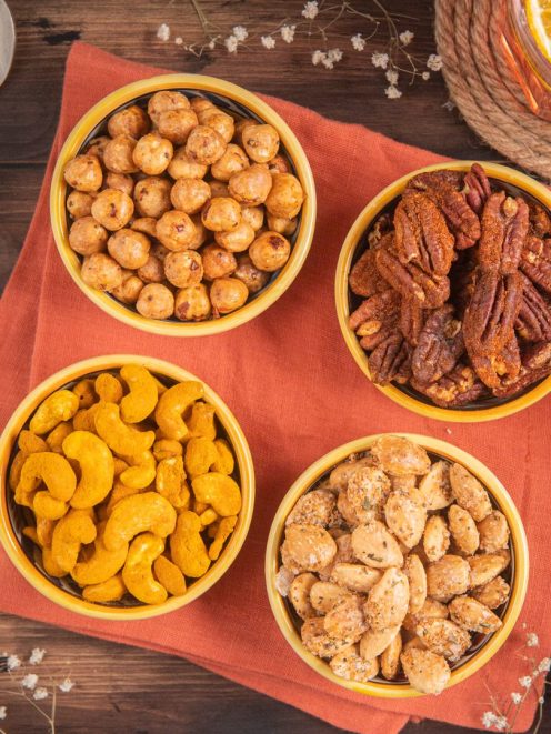 Frutta secca da aperitivo in quattro ciotole con nocciole, pecan speziate, anacardi al curry e mandorle