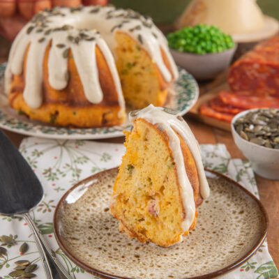 Kugelhopf salato a fette con glassa filante e semi di zucca, salame piccante e piselli sullo sfondo