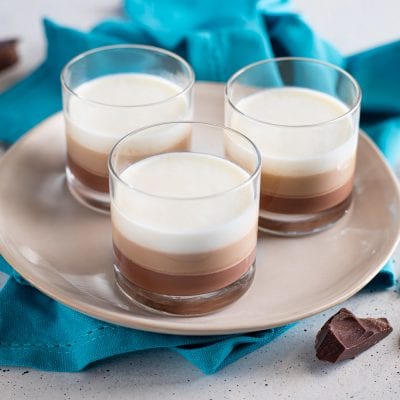 Panna cotta ai tre gusti servita in bicchieri con strati di cioccolato fondente, al latte e panna