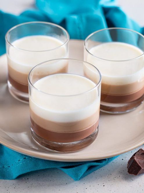 Panna cotta ai tre gusti servita in bicchieri con strati di cioccolato fondente, al latte e panna