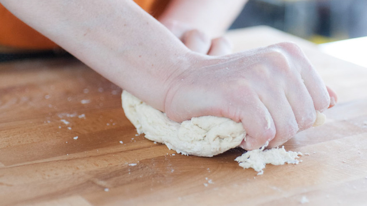 Mani che lavorano energicamente un panetto di pasta fresca sul piano infarinato