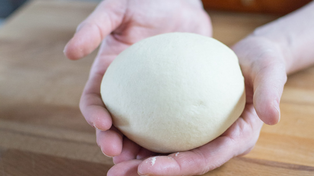 Mani che reggono una palla di impasto liscia e ben lavorata