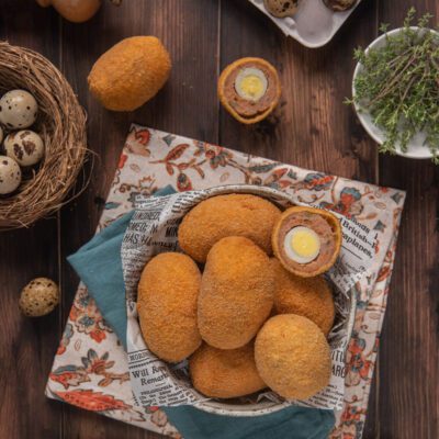 Uova alla scozzese fritte con panatura dorata, uno tagliato a metà rivela l'uovo di quaglia interno