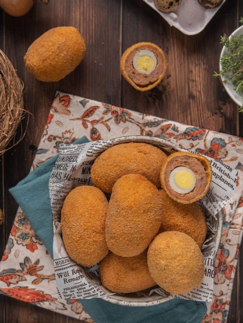 Uova alla scozzese fritte con panatura dorata, uno tagliato a metà rivela l'uovo di quaglia interno