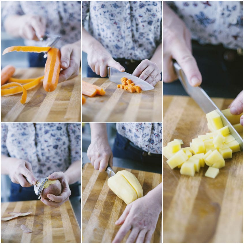 Mani che pelano e tagliano a cubetti carote e patate su un tagliere di legno
