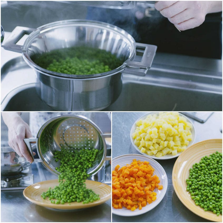 Piselli lessati scolati in un colapasta, accanto a dadini di patate e carote già cotti