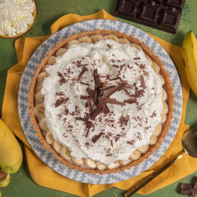 Banoffee pie con banane a rondelle, panna montata e scaglie di cioccolato fondente sulla superficie