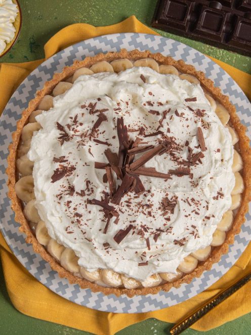 Banoffee pie con banane a rondelle, panna montata e scaglie di cioccolato fondente sulla superficie