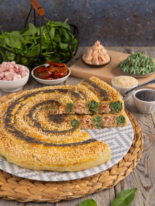Chiocciola salata ripiena a spirale con prosciutto, spinaci e pomodori secchi, coperta di semi di sesamo e papavero