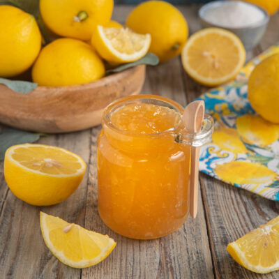 Marmellata di limoni in vasetto aperto con cucchiaino, circondata da limoni freschi tagliati