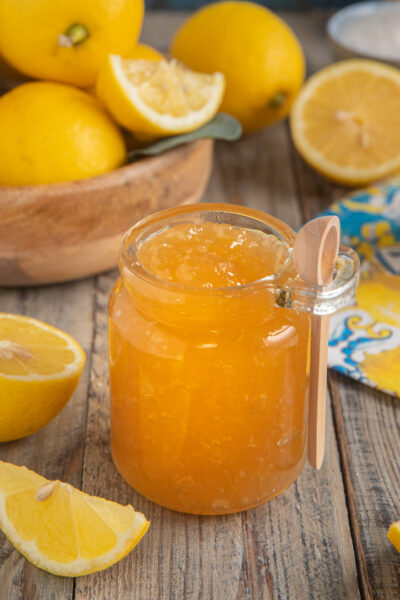 Marmellata di limoni in vasetto aperto con cucchiaino, circondata da limoni freschi tagliati