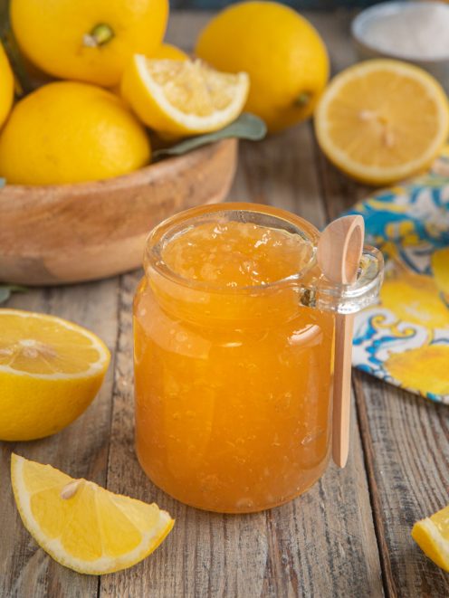 Marmellata di limoni in vasetto aperto con cucchiaino, circondata da limoni freschi tagliati