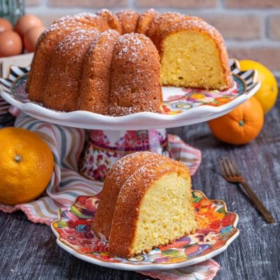 Pan d'arancia a ciambella spolverato di zucchero a velo, con una fetta tagliata e arance fresche accanto