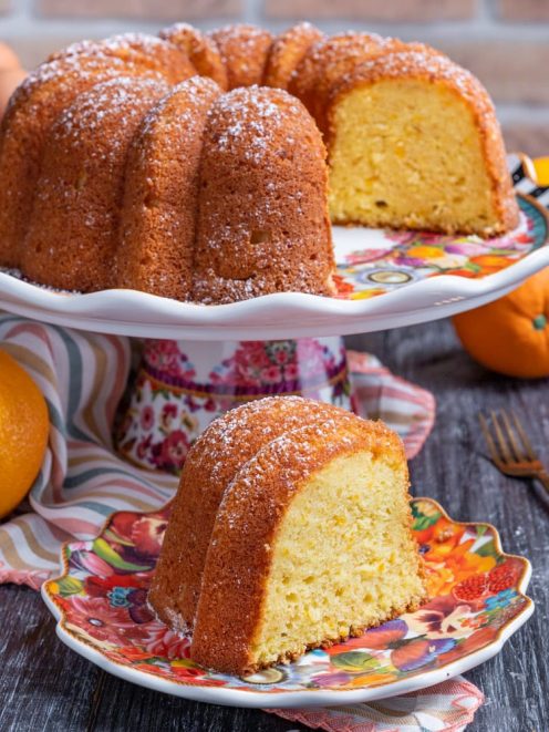 Pan d'arancia a ciambella spolverato di zucchero a velo, con una fetta tagliata e arance fresche accanto