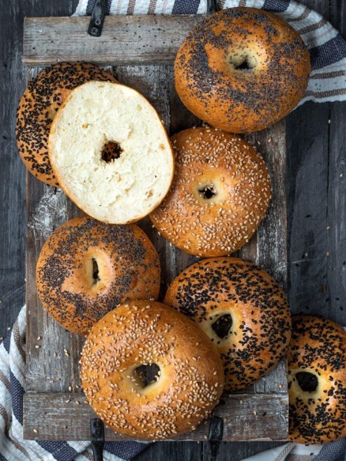Bagel appena sfornati con semi di sesamo e papavero, uno tagliato a metà