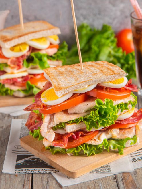 Club sandwich a strati con pollo, bacon croccante, uovo sodo, pomodoro e lattuga farcito tra fette di pane tostato