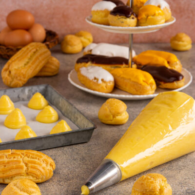 Bignè di pasta choux glassati al cioccolato e zucchero, con eclair e sac à poche di crema pasticcera