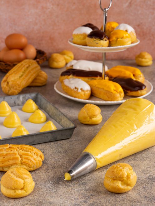 Bignè di pasta choux glassati al cioccolato e zucchero, con eclair e sac à poche di crema pasticcera