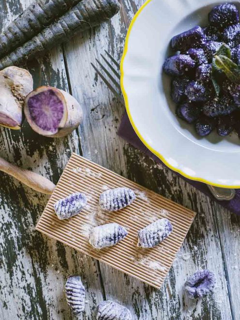 Gnocchi di patate e carote viola rigati, crudi sul rigagnocchi e cotti nel piatto con salvia