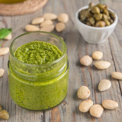 Pesto di capperi in vasetto di vetro, con mandorle e capperi interi sparsi intorno