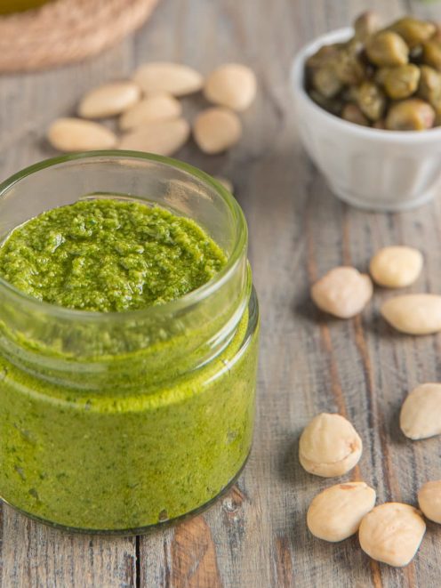 Pesto di capperi in vasetto di vetro, con mandorle e capperi interi sparsi intorno