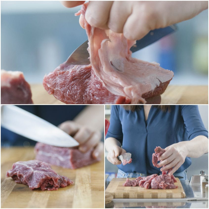 Mani che rimuovono il grasso dal manzo crudo e lo tagliano a striscioline sul tagliere