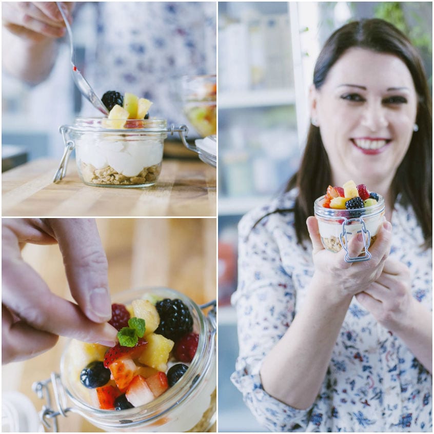 Mani che dispongono frutta mista e menta su strati di yogurt e granola in un barattolo