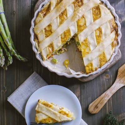 Quiche alle verdure con copertura a griglia dorata, una fetta servita a parte con asparagi freschi