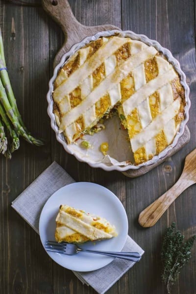 Quiche alle verdure con copertura a griglia dorata, una fetta servita a parte con asparagi freschi