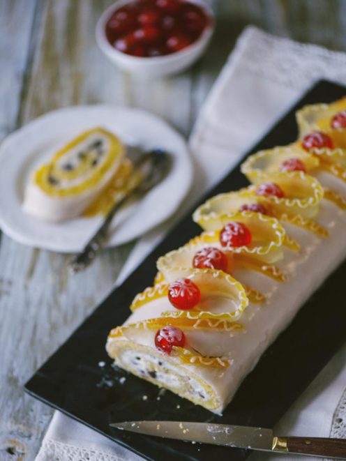 Rotolo di cassata glassato con scaglie di ghiaccia colorata e ciliegine candite in fila
