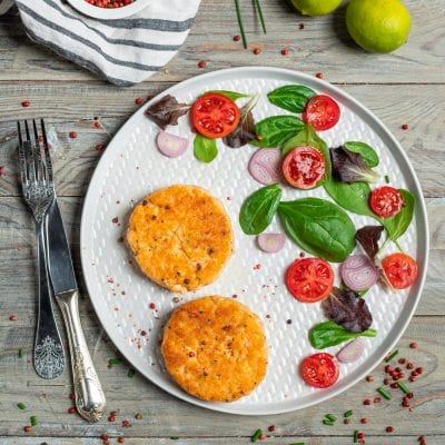Medaglioni di salmone dorati serviti con insalata mista, pomodorini e cipolla rossa