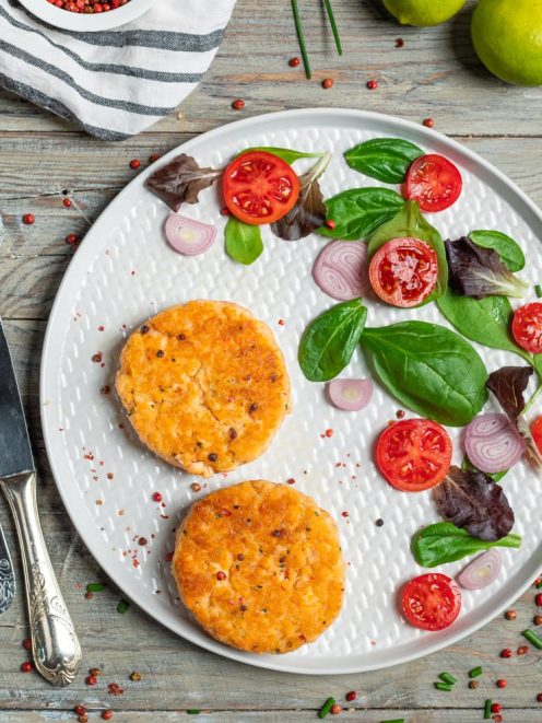 Medaglioni di salmone dorati serviti con insalata mista, pomodorini e cipolla rossa