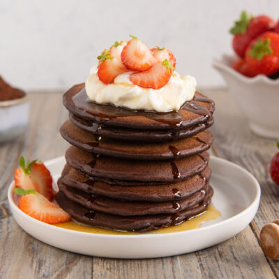 Pancakes al cacao impilati con panna, fragole fresche e miele colante