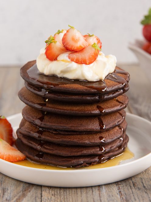 Pancakes al cacao impilati con panna, fragole fresche e miele colante