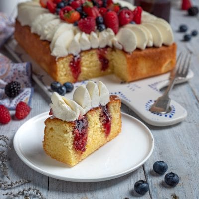 Poke cake farcita con confettura di frutti rossi, panna e fragole fresche in cima
