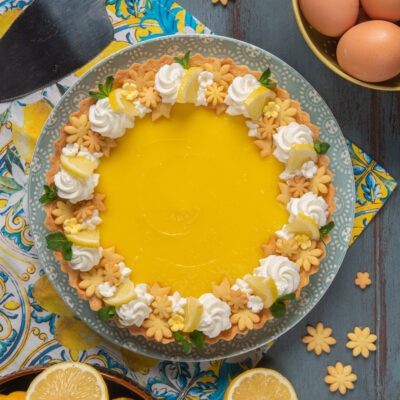 Tarte al lemon curd con crema al limone, ciuffi di panna, biscottini a fiore e fettine di limone