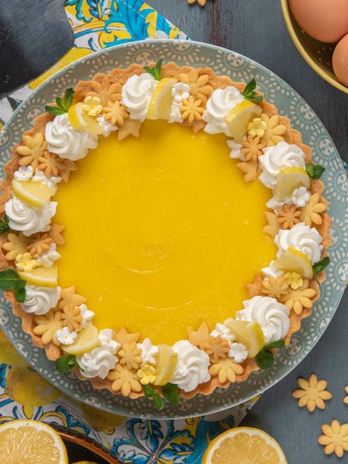 Tarte al lemon curd con crema al limone, ciuffi di panna, biscottini a fiore e fettine di limone