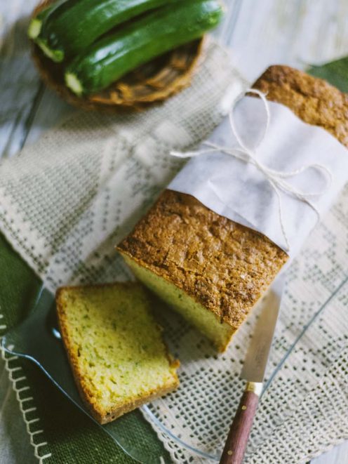 Zucchini bread affettato con mollica verde e crosta dorata, accanto a zucchine fresche