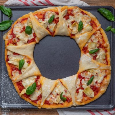 Ghirlanda di pizza con salsa di pomodoro, carciofi, mozzarella filante e foglie di basilico fresco