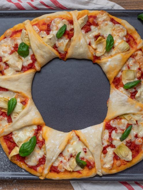 Ghirlanda di pizza con salsa di pomodoro, carciofi, mozzarella filante e foglie di basilico fresco