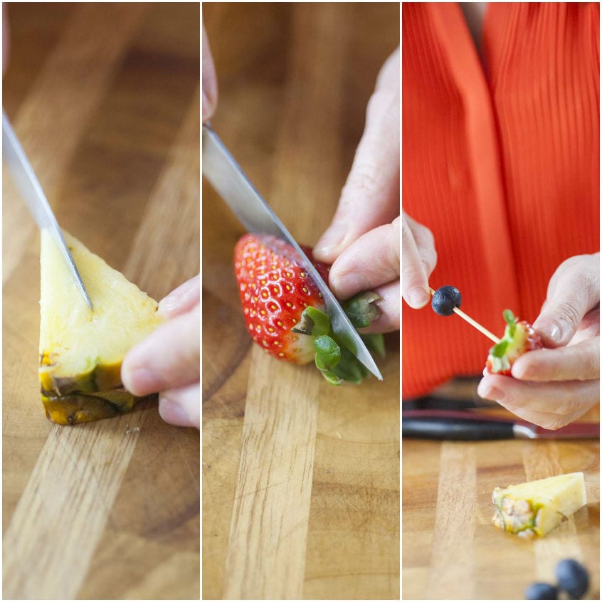 Mani che tagliano ananas e fragola, poi infilzano mirtillo e fragola su uno stecchino