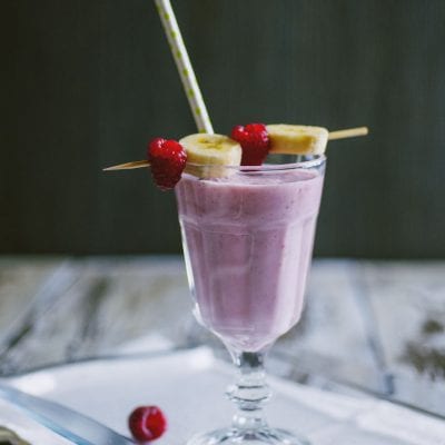 Frappè di banane e lamponi guarnito con fettine di banana e lamponi freschi su spiedino